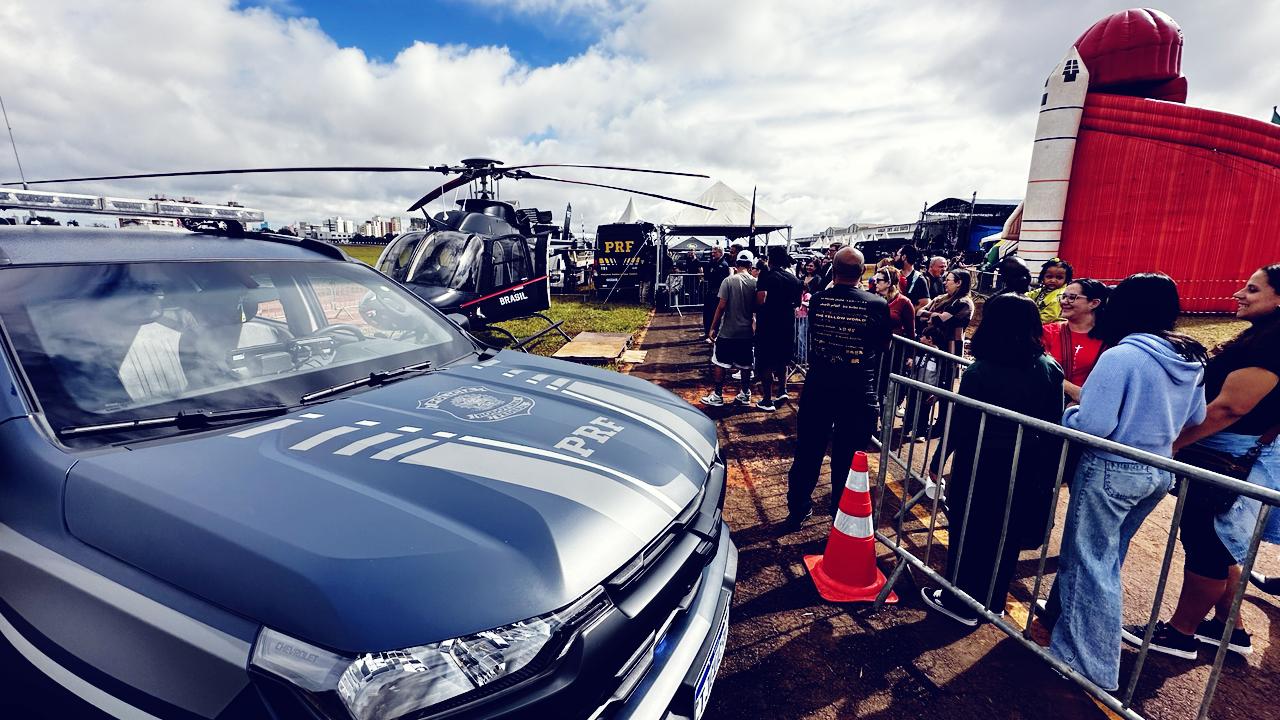 Visitantes observam viatura e helicóptero da PRF expostos durante evento aberto ao público, em área