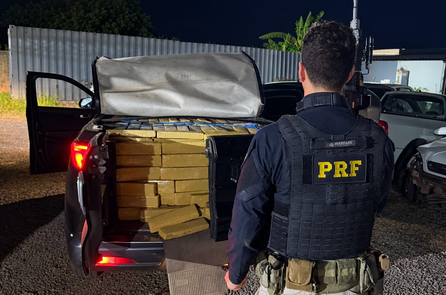 A imagem mostra um agente da PRF olhando para uma caminhonete com drogas