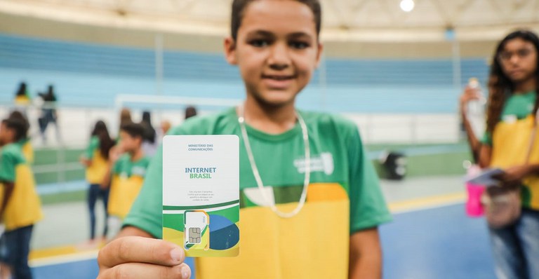 Criança com uniforme de escola mostra cartão com chip do Programa Internet Brasil, que distribui os chips para alunos da educação básica terem acesso à internet