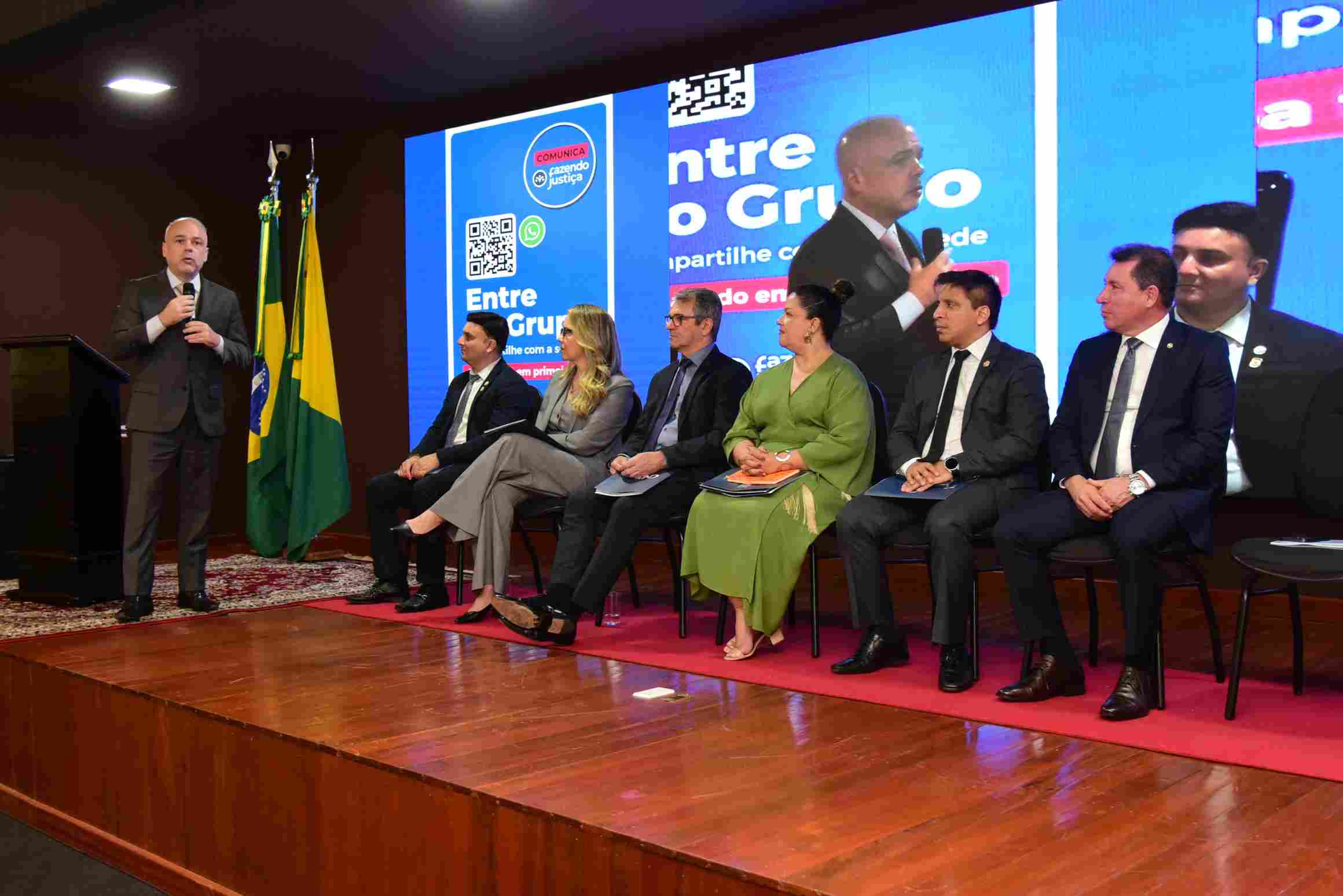 Pessoas sentadas em fileira com telão de fundo