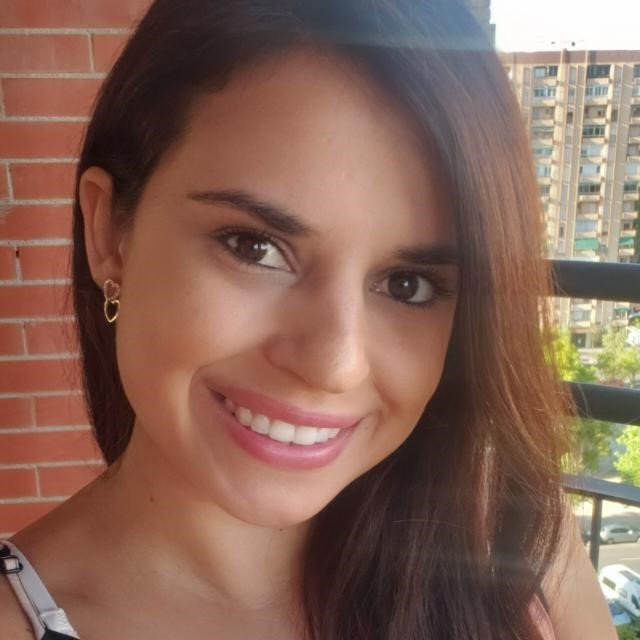 mulher branca, cabelos lisos, longos e castanho claros. Sorri para a foto e está na varanda de um ´apartamento.