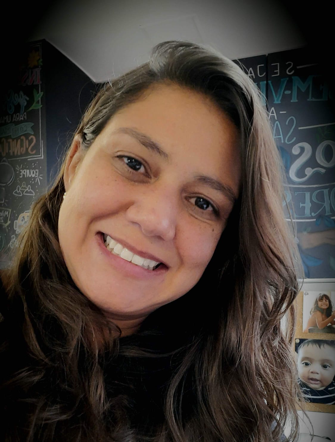 mulher parda de cabelos lisos longos. sorri para foto e veste uma blusa preta.