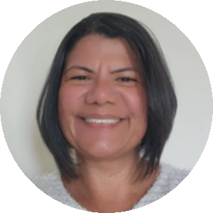 Mulher de cabelo curto e liso, sorrindo em frente a um fundo claro. Ela veste uma blusa clara de textura felpuda e transmite uma expressão acolhedora e simpática.