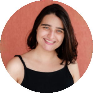 . Foto de Paloma Abelin, mulher branca de olhos verdes, cabelos lisos e escuros até o ombro. Ela veste uma blusa de alça preta e sorri.