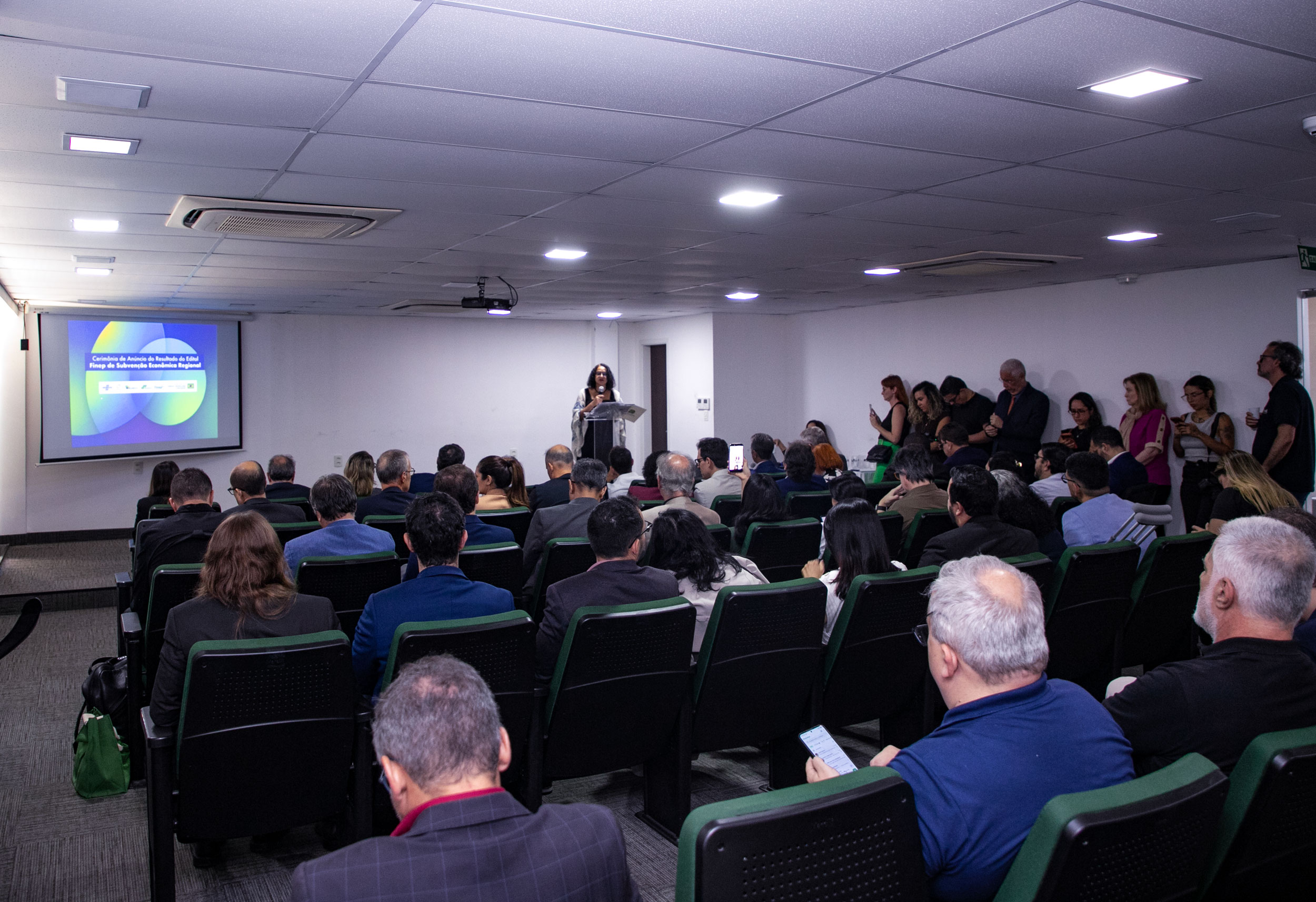 Foto da Ministra Luciana Santos diante de um púlpito falando para um auditório lotado