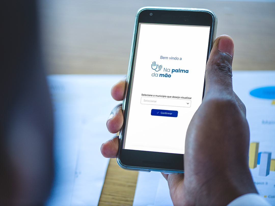 Homem segurando um smartphone com a tela exibindo o aplicativo "Na Palma da Mão"