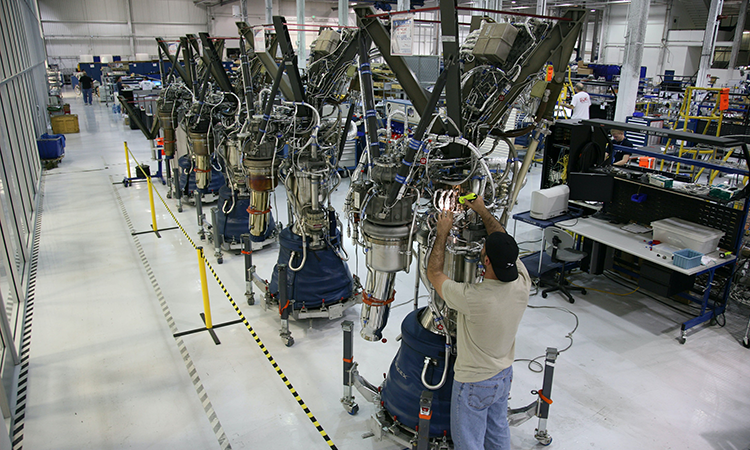 Foto de um trabalhador em linha de montagem de equipamento espacial.