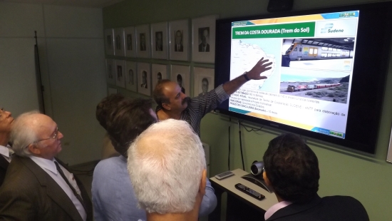Superintendente Zé Marcio mostrando apontando para uma ilustração na televisão e outras quatro pessoas olhando.