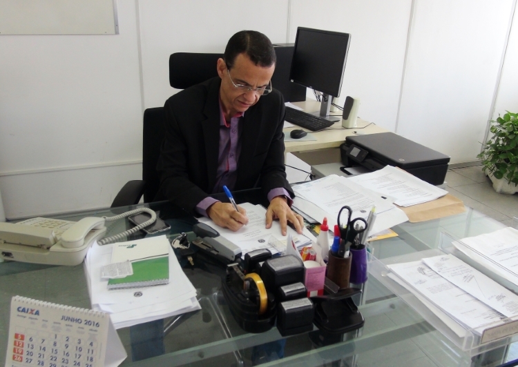 Foto do diretor de planejamento da Sudene, Sérgio Alencar, sentado em sua sala assinando um documento.