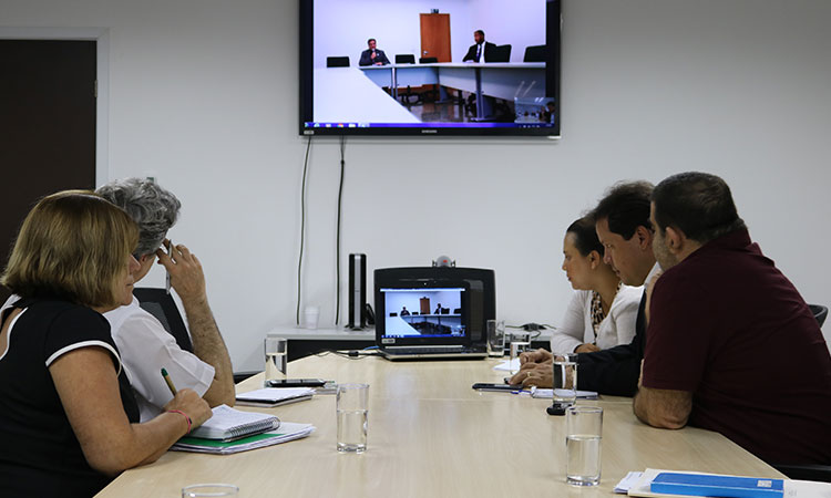 Superintendente Marcelo Neves e técnicos da Autarquia sentados à mesa, na sala de Reuniões JK, durante a videoconferência. Ao fundo a televisão com imagens dos representantes da CNA.