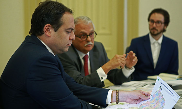 Paulo Câmara, Mário Gordilho e Renato Oliveira (engenheiro da Sudene) sentados à mesa de reunião. O governador está com  o palno na mão.
