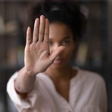 Foto de uma mulher negra, de frente, com a mão espalmada. A mão, em primeiro plano, aparece em foco, com o rosto da mulher desfocado ao fundo.