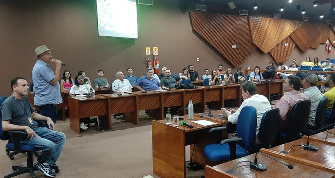 Foto mostra homem de chapéu e em pé falando em evento