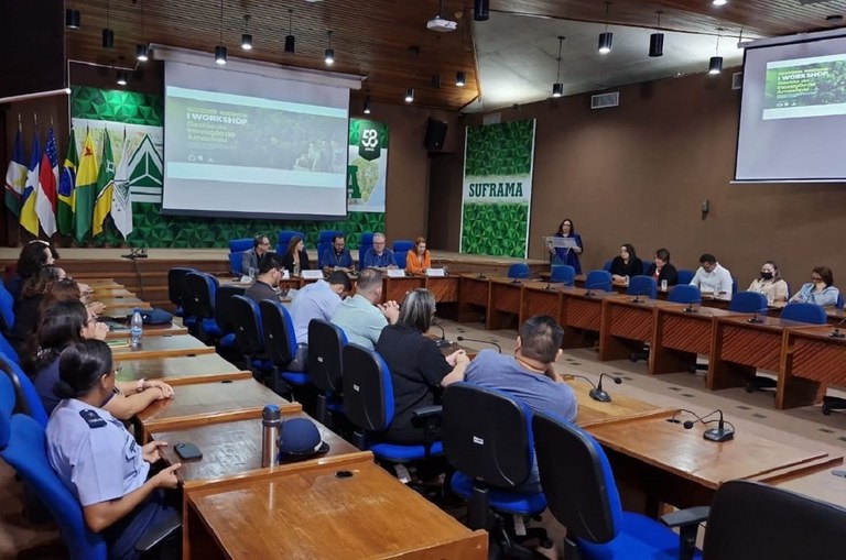 Foto mostra mulher em pé falando junto ao púlpito, num evento institucional