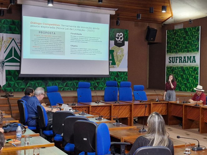 Foto mostra mulher fazendo uma apresentação com um telão de apoio