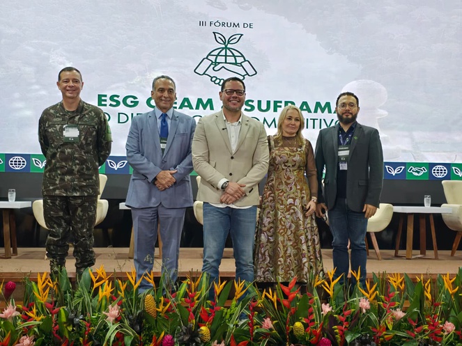 Foto mostra pessoas em pé em frente a um telão