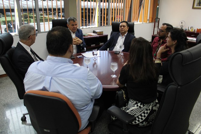 Foto mostra um grupo de pessoas reunidas e ouvindo a explicação de uma delas, um homem que está vestido de paletó azul