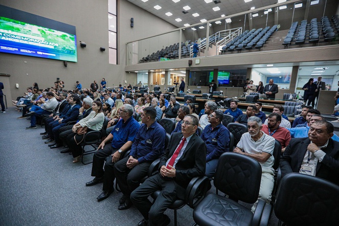 Foto mostra pessoas reunidas em um auditório com telão ao fundo