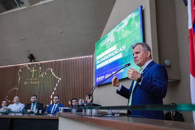 Foto mostra homem de blazer azul falando ao microfone