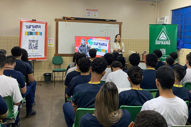 Foto mostra mulher de blusa bege clara, falando a um grupo de estudantes