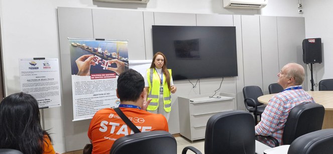 Foto mostra um grupo de pessoas com equipamento de proteção em vista a um porto de cargas