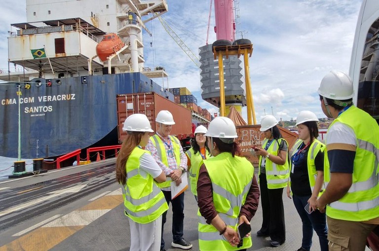 Foto mostra grupo de pessoas com equipamento de proteção em vista a um porto de cargas