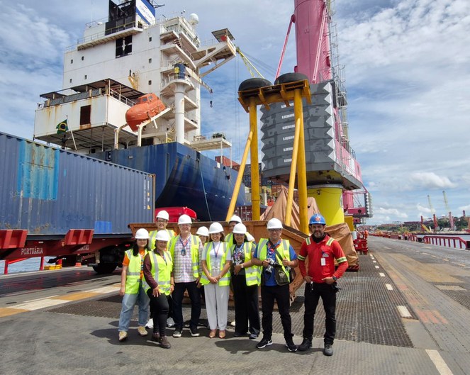Foto mostra um grupo de pessoas com equipamento de proteção em vista a um porto de cargas em Manaus