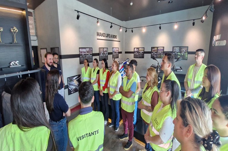 Foto mostra grupo de pessoas com jaleco verde ouvindo uma explanação