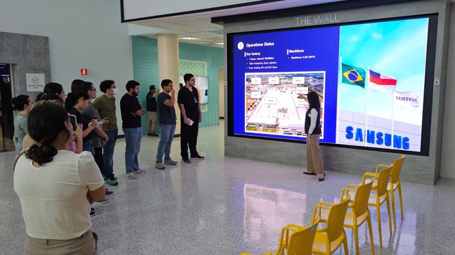 Foto mostra pessoas em frente um telão