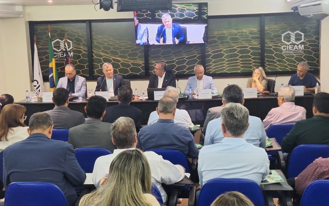 Foto mostra homem falando ao microfone em evento realizado num auditório quase cheio