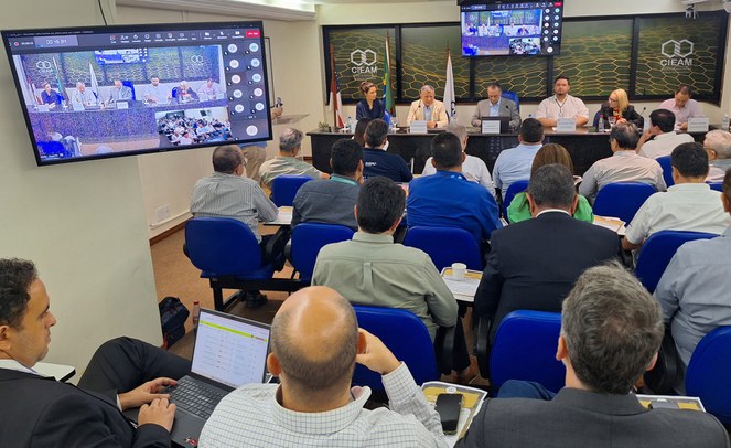 Foto mostra pessoas em reunião num auditório lotado e com imagem da atividade também aparecendo num telão