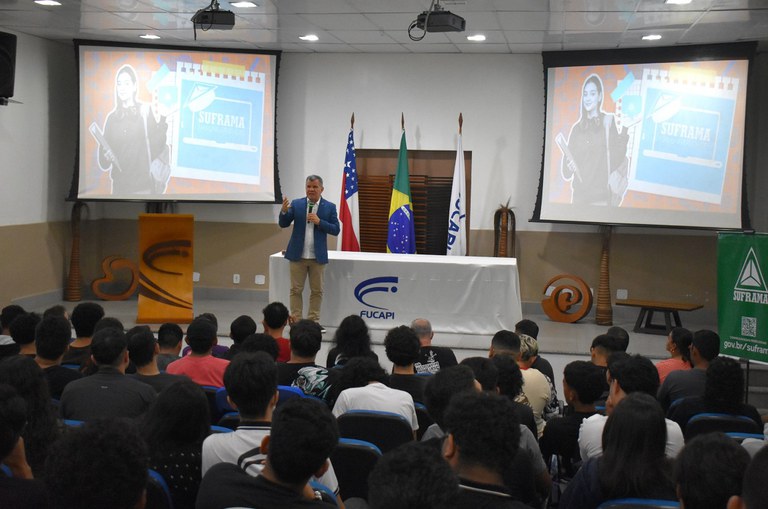 Homem em um palco falando para uma plateia sentada