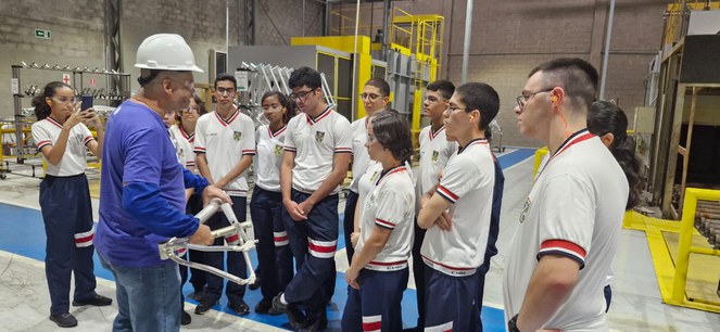 Foto mostra homem com capacete branco mostrando peça de bicicleta a estudantes