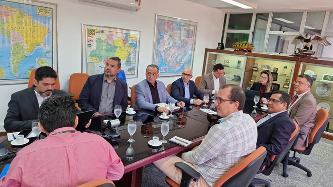 Foto mostra grupo de pessoas em reunião com o apoio de um telão