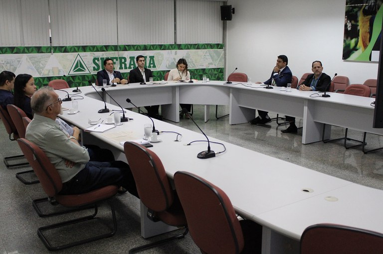 Foto mostra pessoas sentadas à mesas em reunião virtual