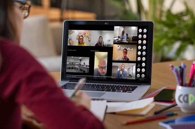 Foto mostra três homens de paletó e uma mulher sentados à mesa numa reunião