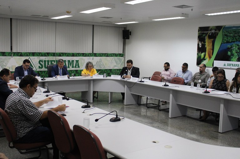 Foto mostra homem de paletó escuro falando ao microfone em uma reunião