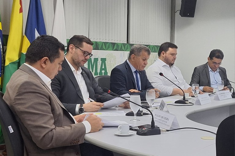 Foto mostra homem fazendo leitura de documentos ao lado de outros homens