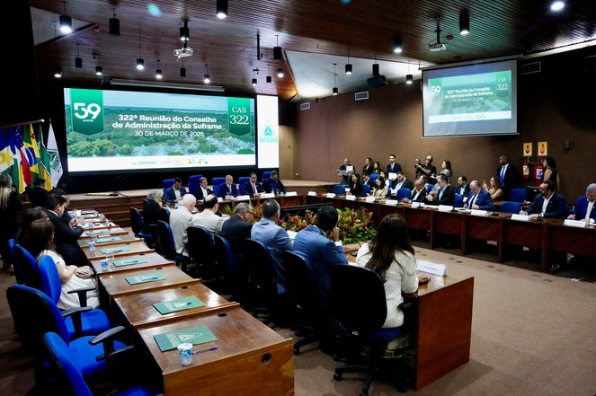 Foto mostra um homem falando ao microfone durante evento e com um telão ao fundo