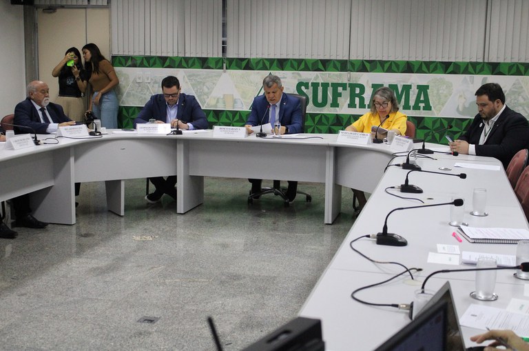 Foto mostra pessoas em uma reunião, com duas jovens ao fundo à esquerda conferindo registro de fotos