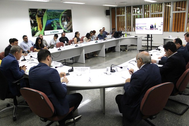 Foto mostra reunião com várias pessoas numa sala amppla