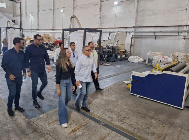 Foto mostra um grupo de pessoas caminhando dentro de uma fábrica