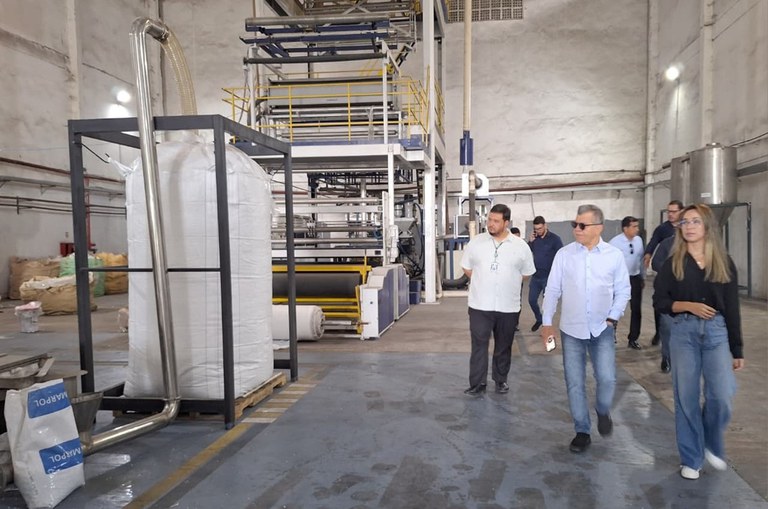 Foto mostra grupo de pessoas caminhando dentro de uma fábrica