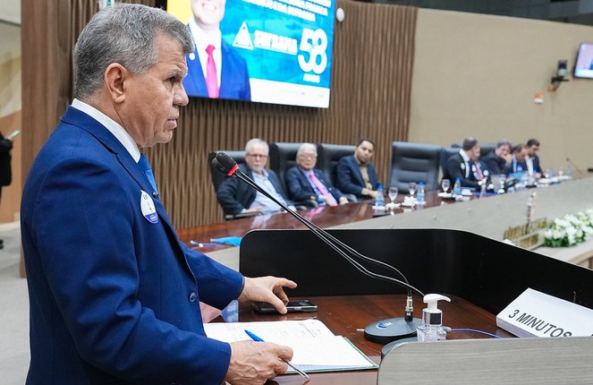 Foto mostra homem de paletó azul falando em um evento público