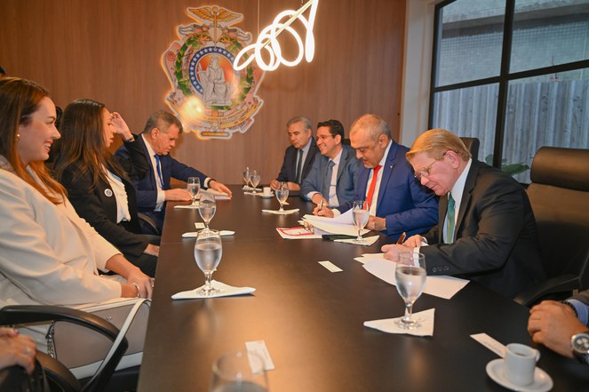 Foto mostra grupo de pessoas sentadas à mesa e observando documentos