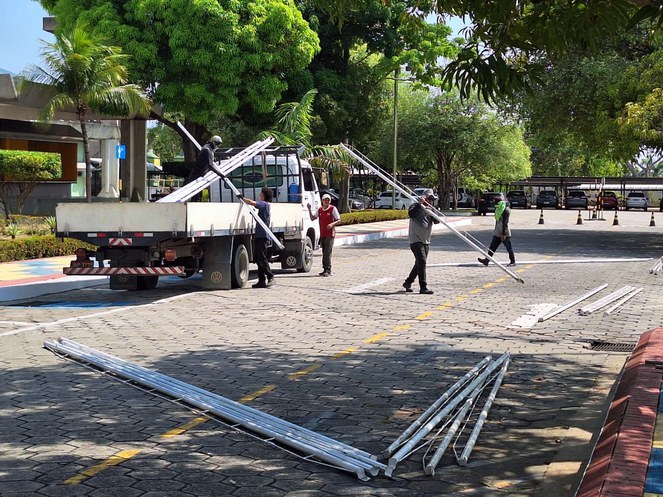 Foto mostra homens carregando peças para erguer tendas para um evento