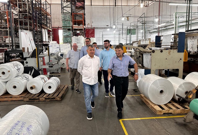Foto mostra grupo de homens andando em uma fábrica de embalagens plásticas