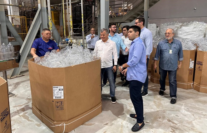 Foto mostra homem de blusa azul mostrando produtos de itens da linha de limpeza a grupo de pessoas