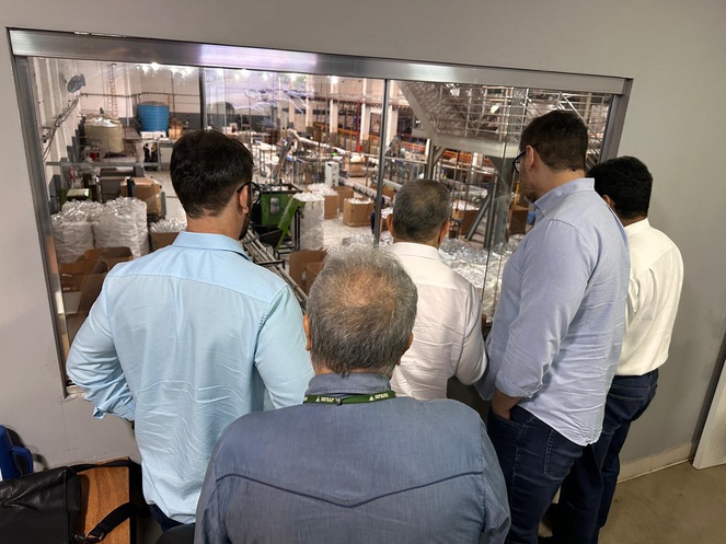 Foto mostra pessoas olhando para produtos da linha de limpeza em uma fábrica