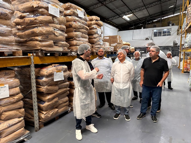 Foto mostra homens com bata e touca em meio pacotes alimentícios